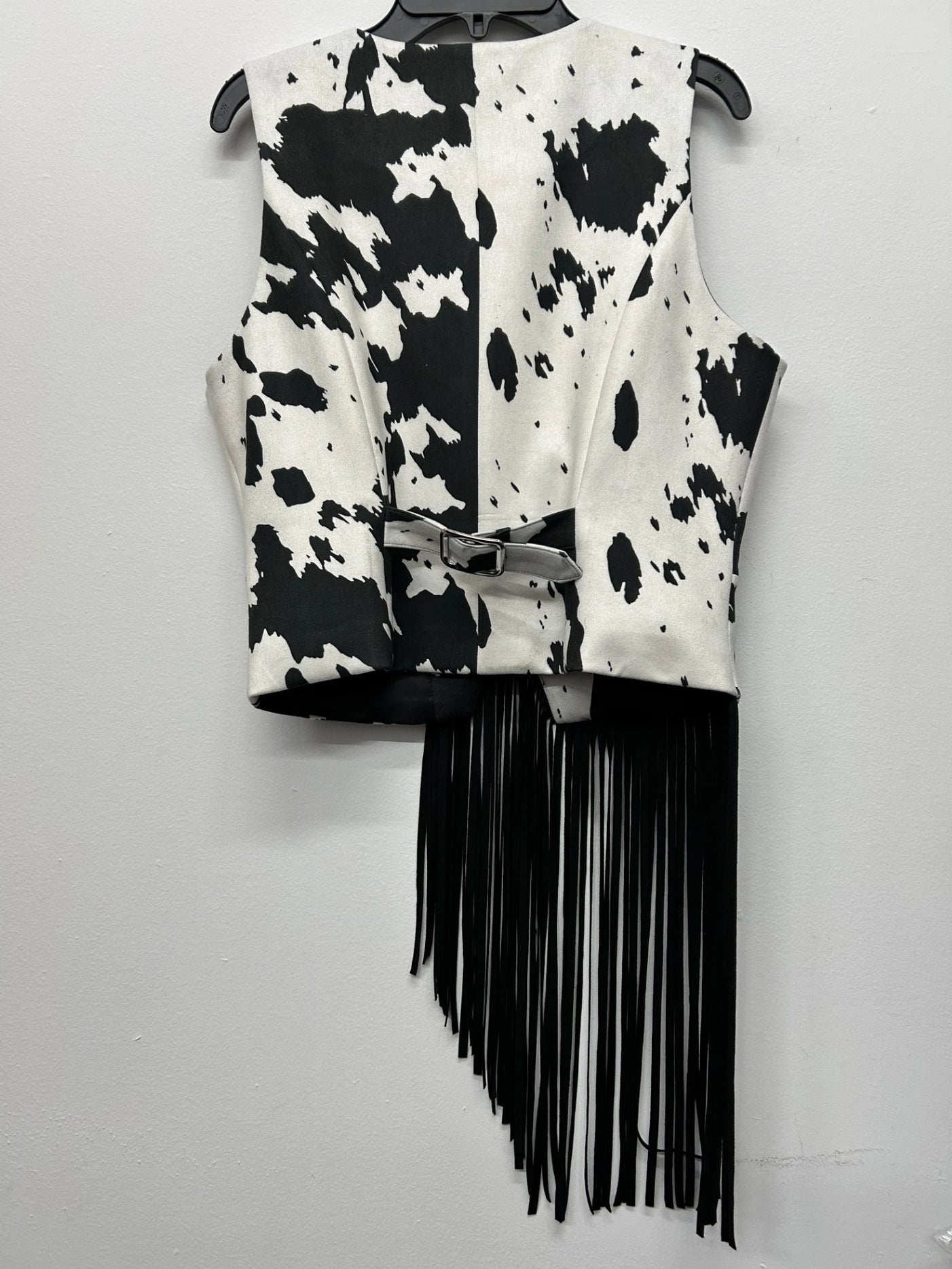 Black and white cow print vest with fringe on a gray background