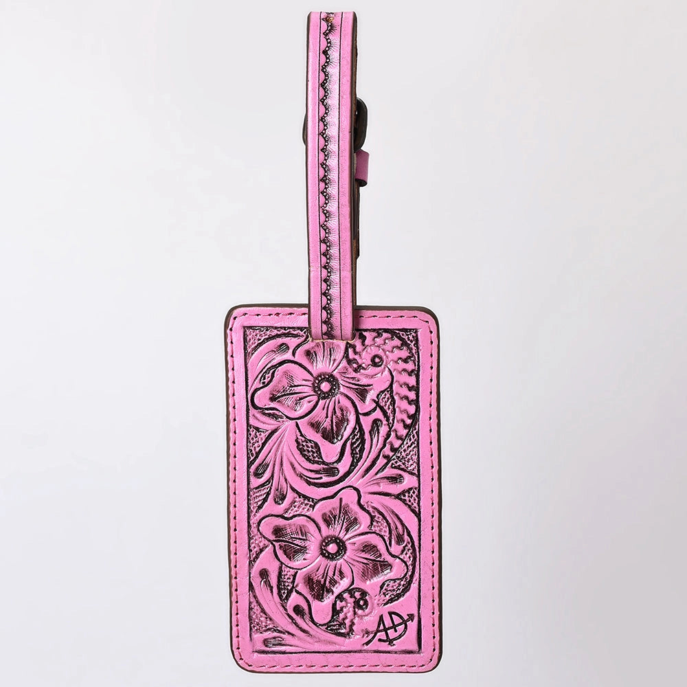 A pink leather luggage tag with hand-tooled floral patterns and a matching pink strap, shown against a plain white background.