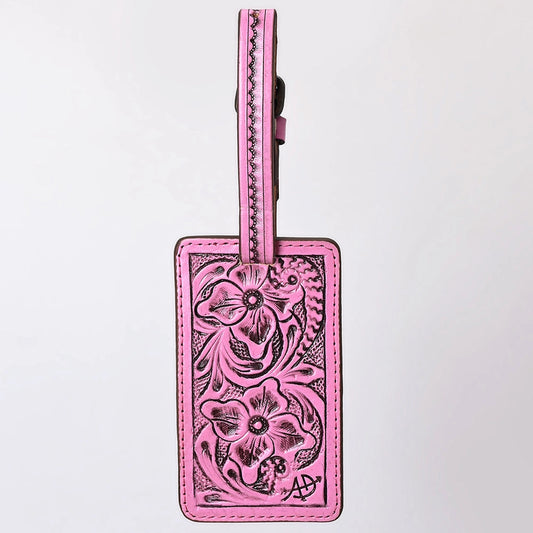 A pink leather luggage tag with hand-tooled floral patterns and a matching pink strap, shown against a plain white background.