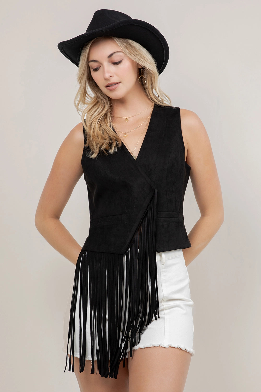 Woman wearing a black fringe vest and white shorts with a plain background