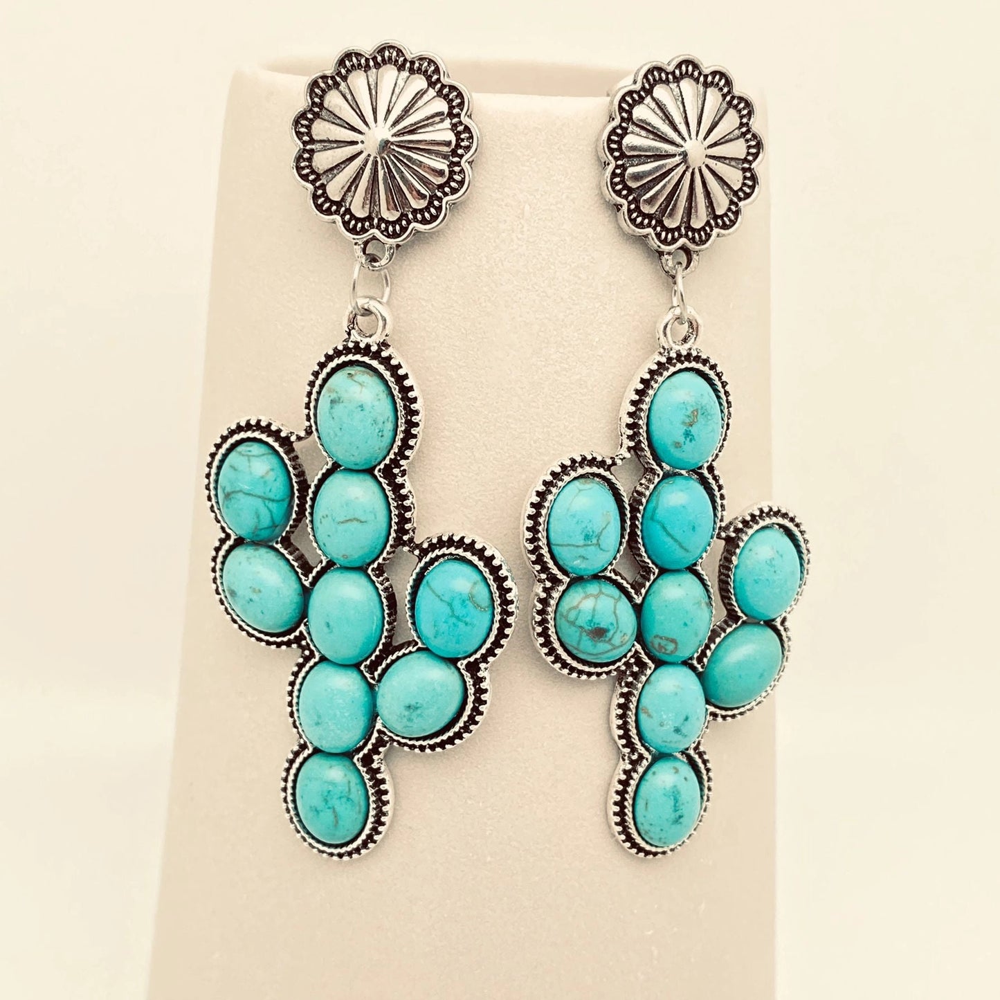 Turquoise and silver cactus shape earrings on a beige background.