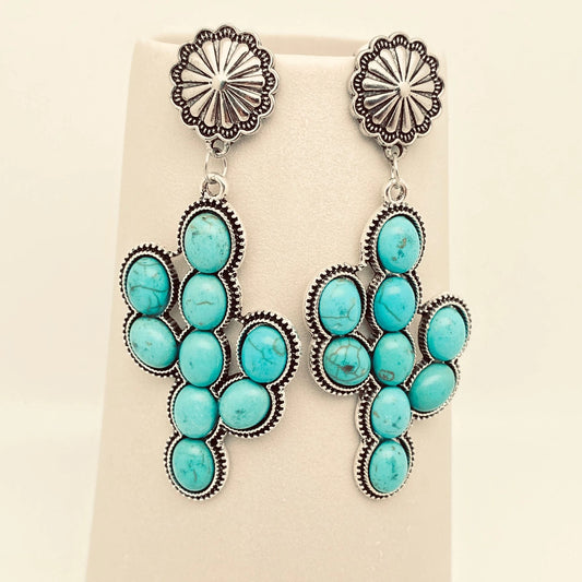 Turquoise and silver cactus shape earrings on a beige background.