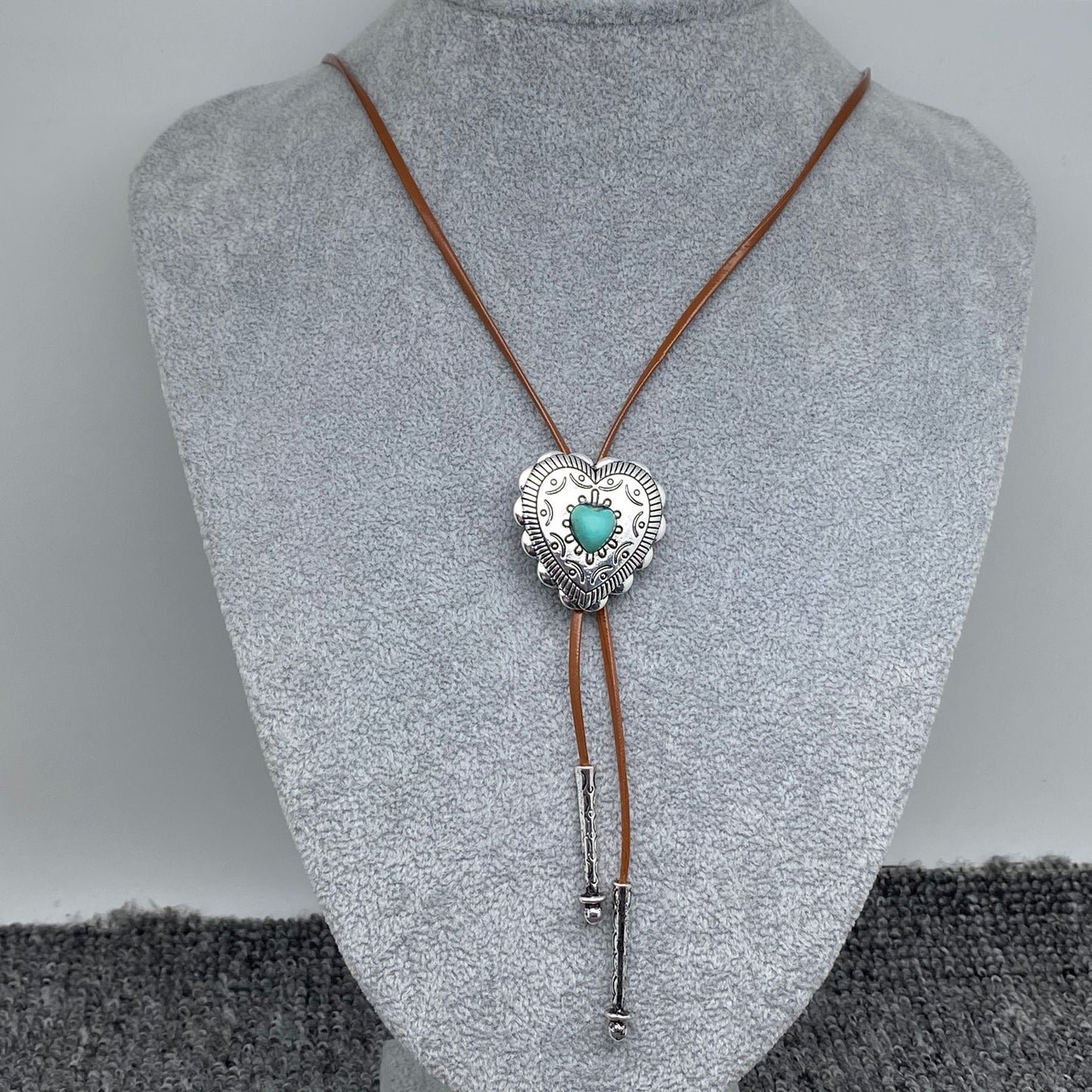 Bolo tie with heart and turquoise stone on a mannequin bust against a grey background
