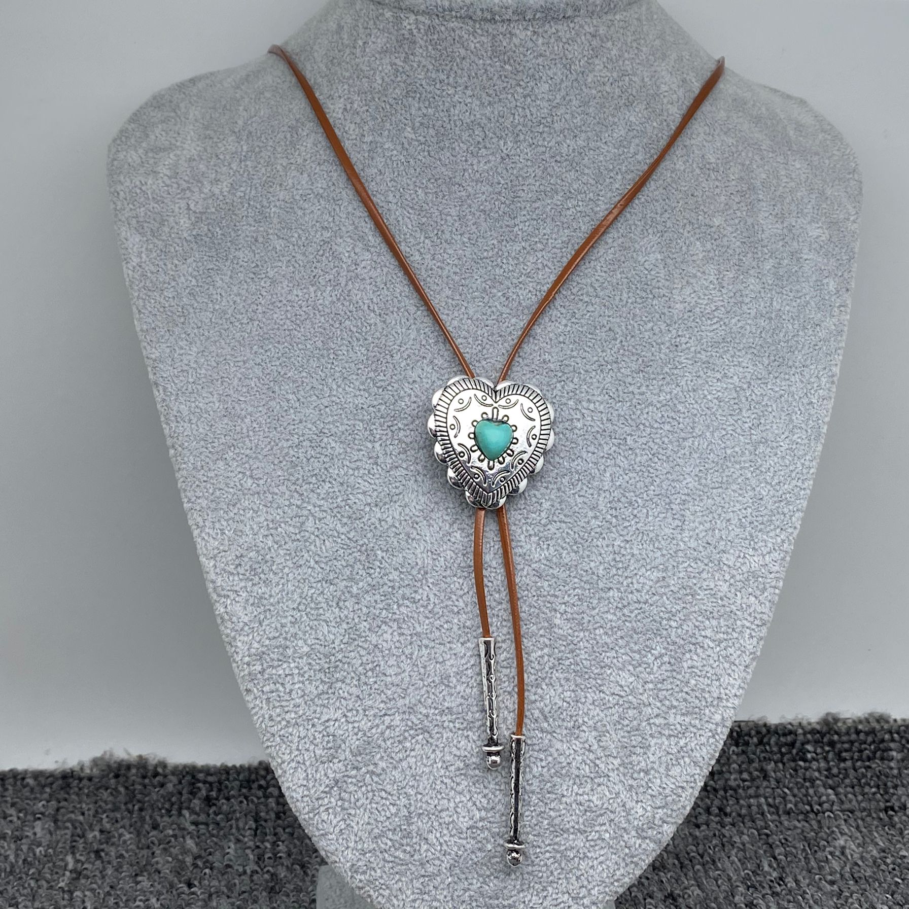 Bolo tie with heart and turquoise stone on a mannequin bust against a grey background