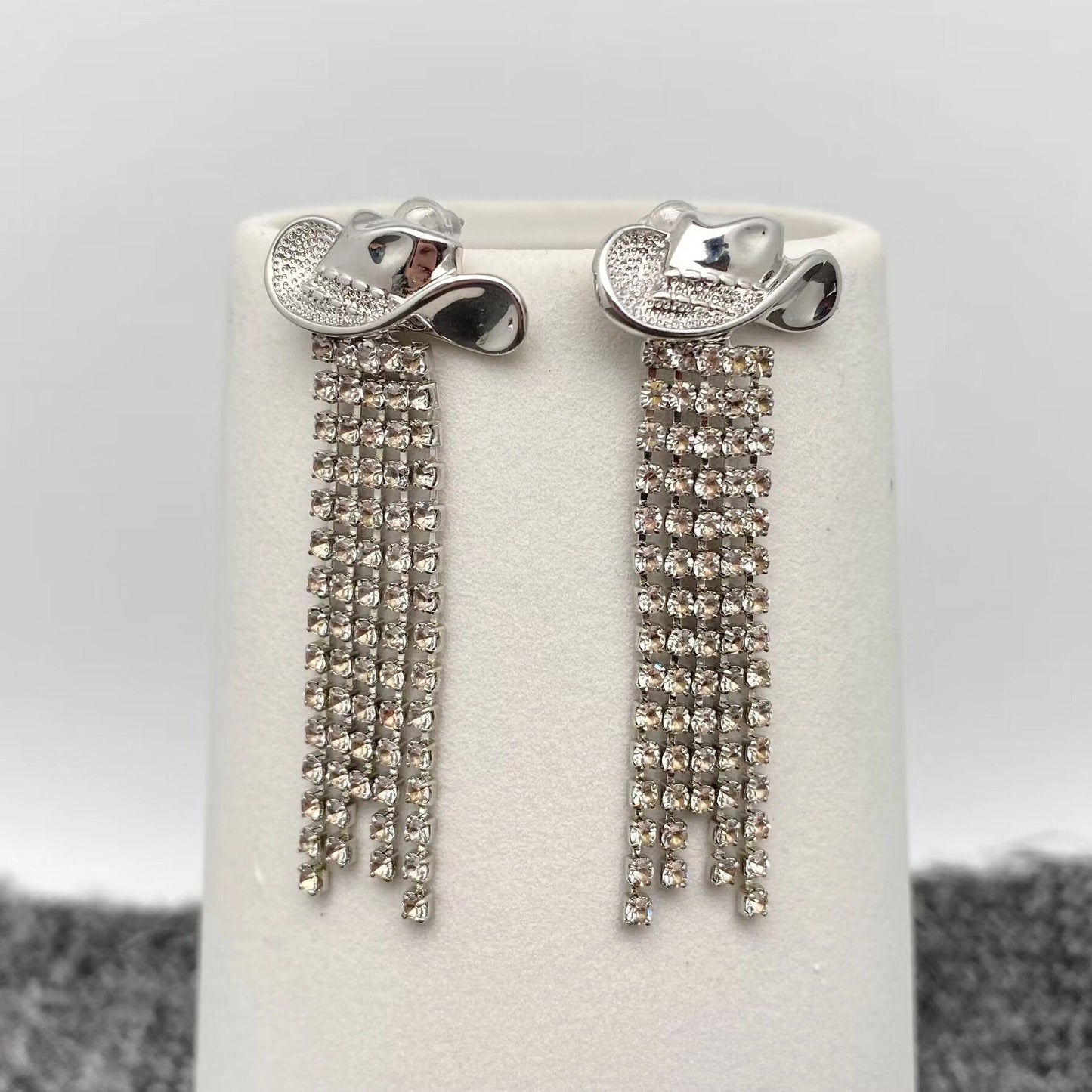 Silver earrings with dangling crystals on a white stand against a grey background