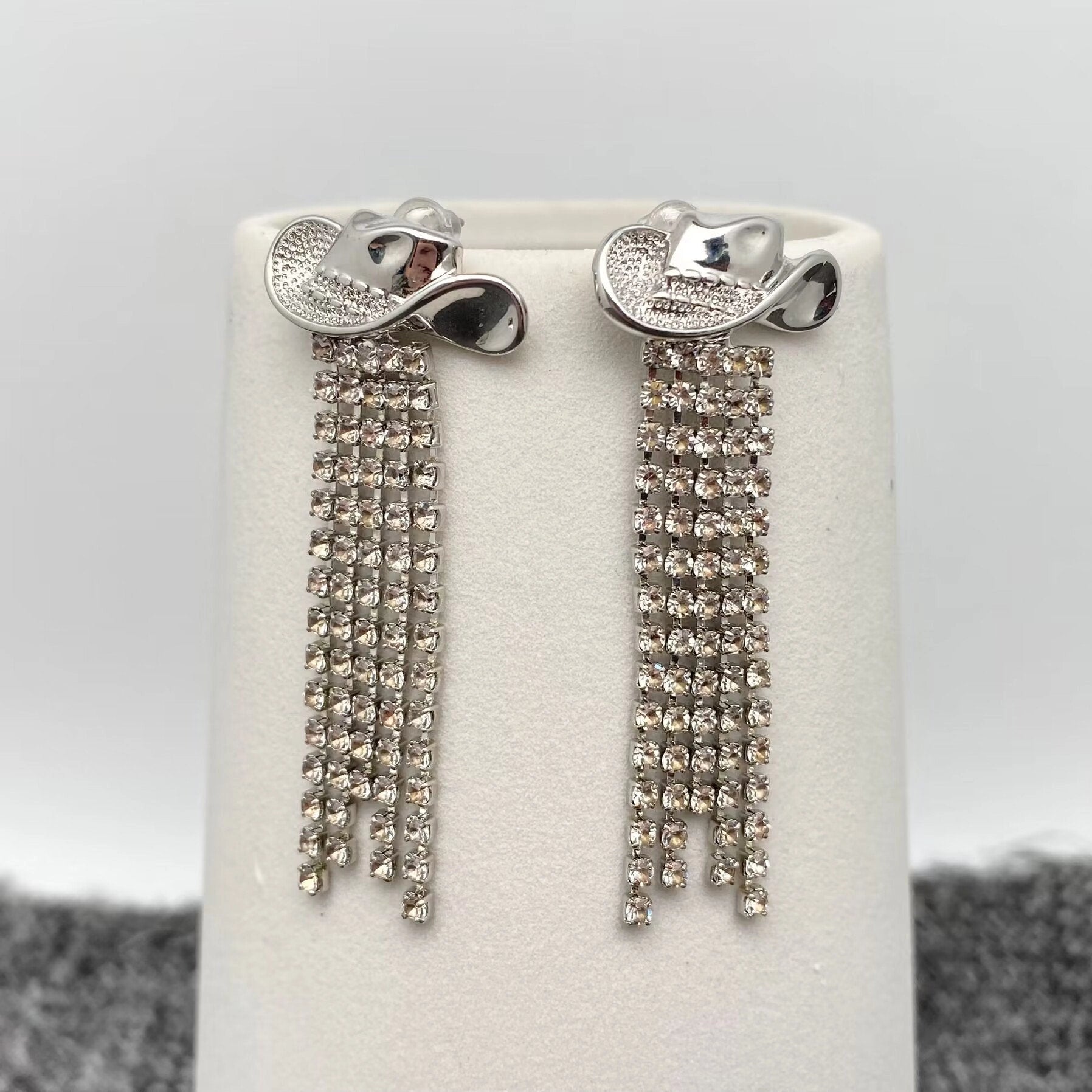 Silver earrings with dangling crystals on a white stand against a grey background