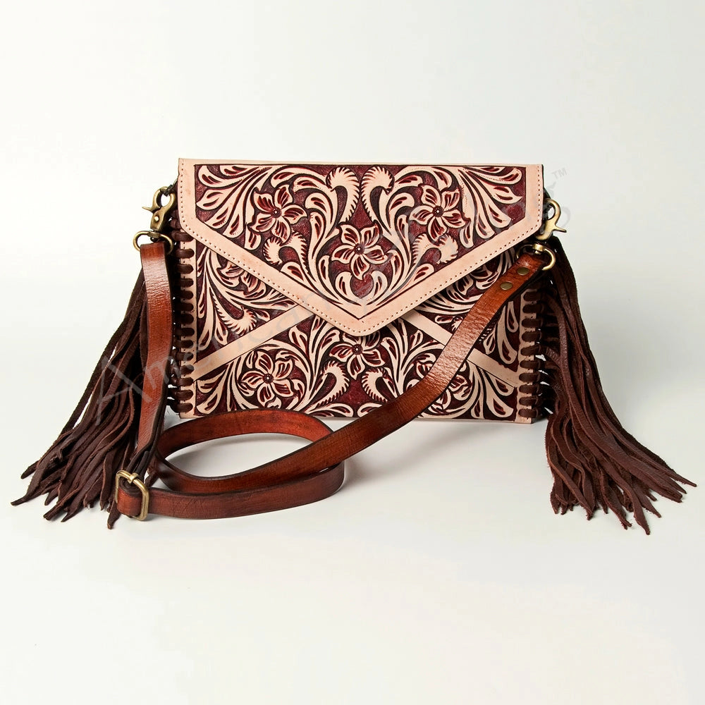 A tooled leather crossbody bag with floral engravings in reddish-brown and beige, featuring long brown leather tassels and a matching brown shoulder strap, shown on a light gray background.