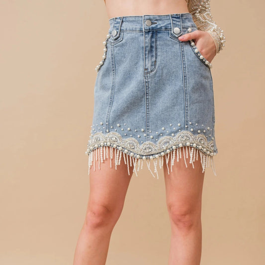 Denim skirt with lace and pearl fringe trim worn by a person on a beige background