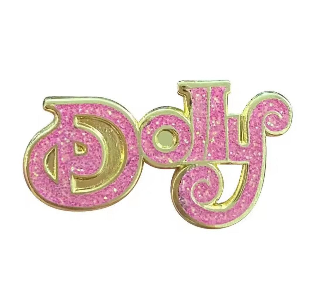 A pink glitter enamel pin spelling out 'Dolly' in a cursive font, outlined in gold metal, shown on a plain white background.