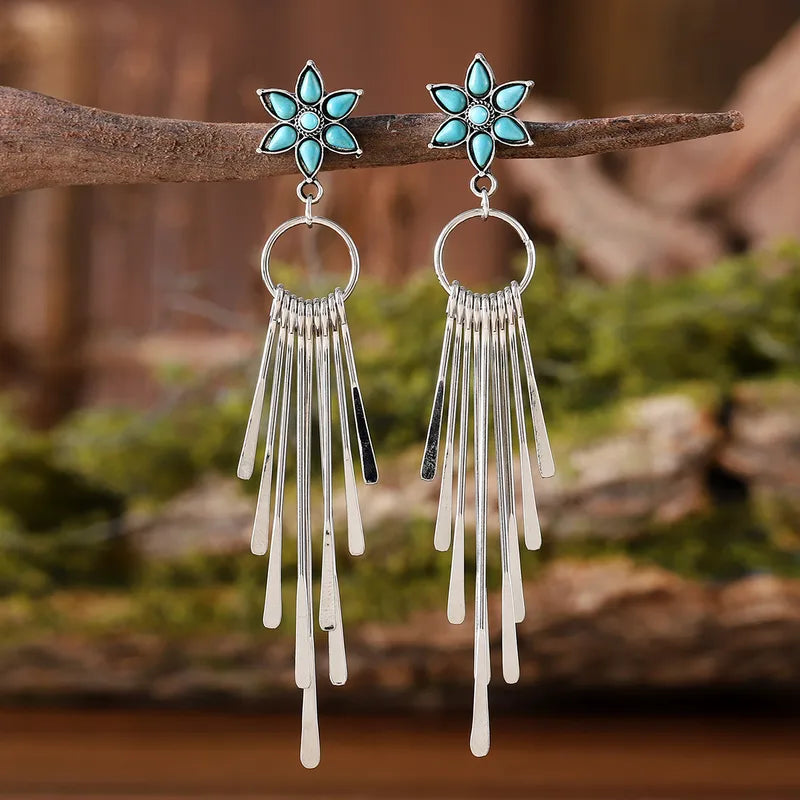 Pair of earrings with turquoise flower tops and silver fringe on a natural background