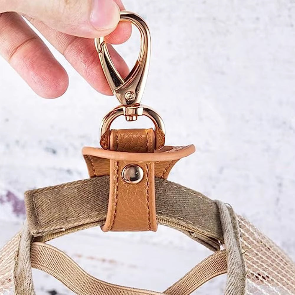 Close-up of a hand holding a keychain or bag charm with a strap to hold baseball cap against a light background