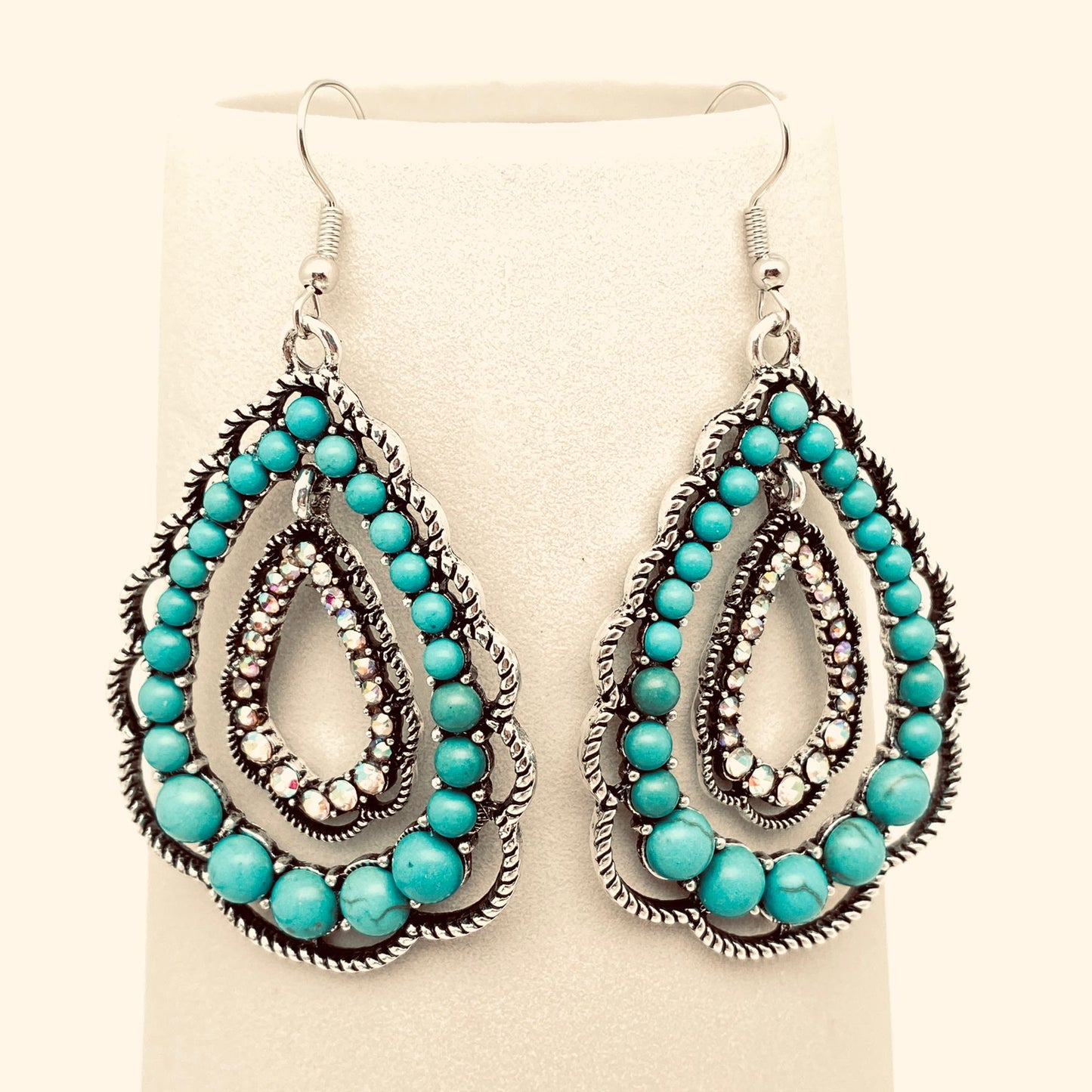 Turquoise beaded and rhinestone earrings on a beige background