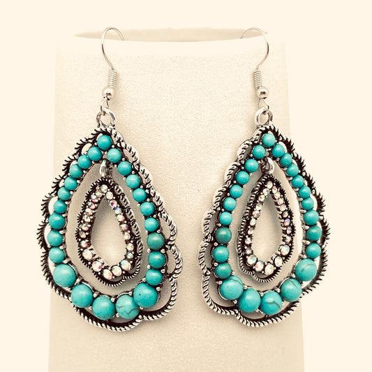 Turquoise beaded and rhinestone earrings on a beige background