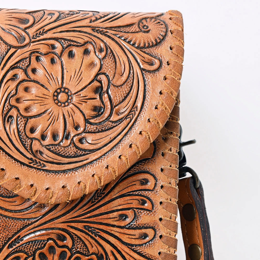 Close-up of a brown tooled leather bag with floral and scrollwork embossing, showing the flap closure and fringe detail against a plain white background.