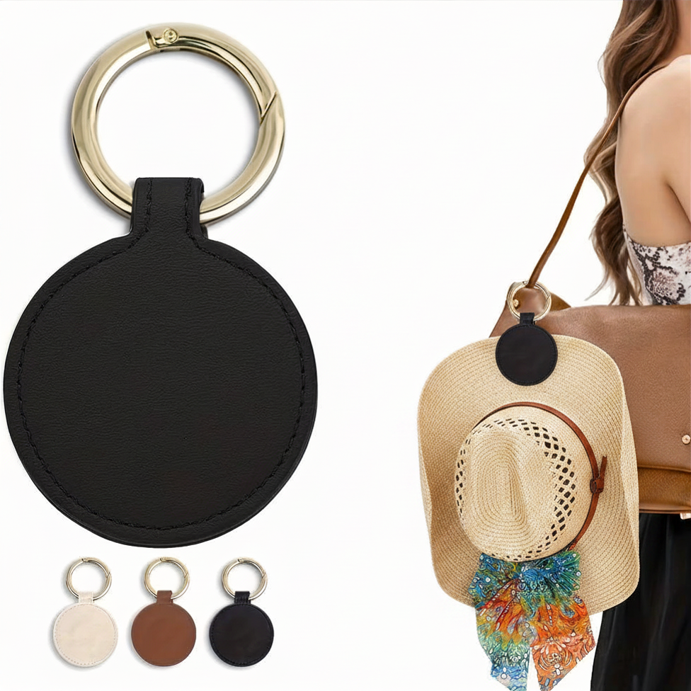 Black round bag clip with gold ring, displayed with a straw hat and handbag on a white background.
