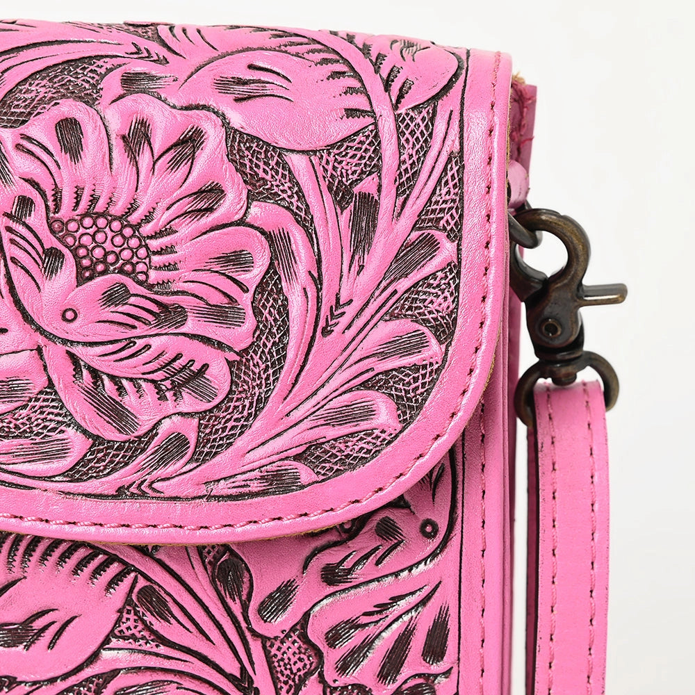 A close-up of a bright pink tooled leather crossbody bag with black floral detailing, a curved flap, and a dark metal clasp on a white background.