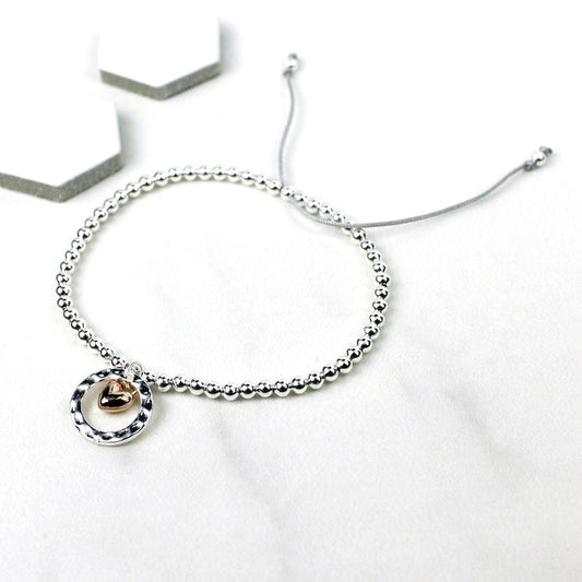 Silver plated beads finished with a textured silver plated ring and a small heart charm in a rose gold finish strung on soft grey cord