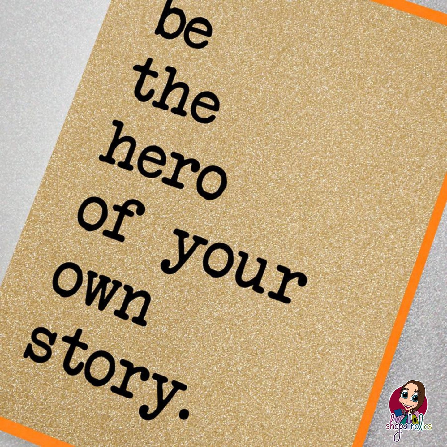 A fabulously sparkly gold glitter effect greeting card featuring the slogan: Be the hero of your own story.